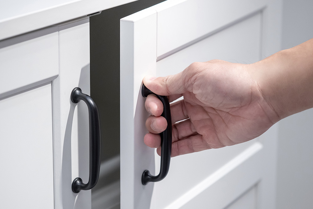 A person opens a white cabinet door using a black handle.