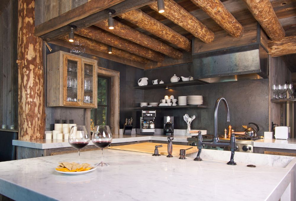 Rustic kitchen with wooden beams, marble counters, wine glasses, and a plate of cheese and crackers.