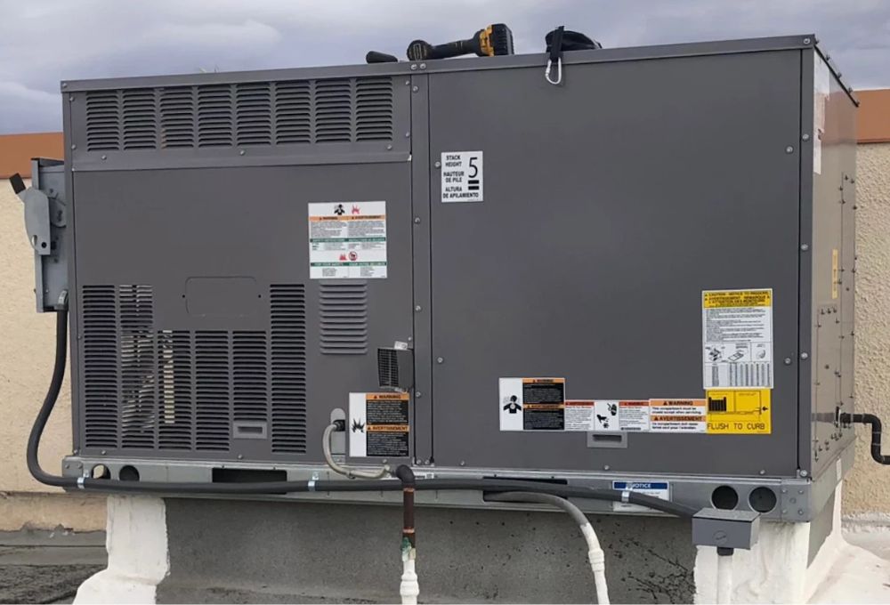 A large gray industrial HVAC unit on a rooftop with multiple warning labels and pipes.