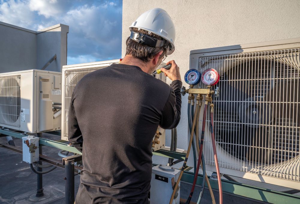 HVAC technician in a hard hat checks gauges on an outdoor condenser unit.