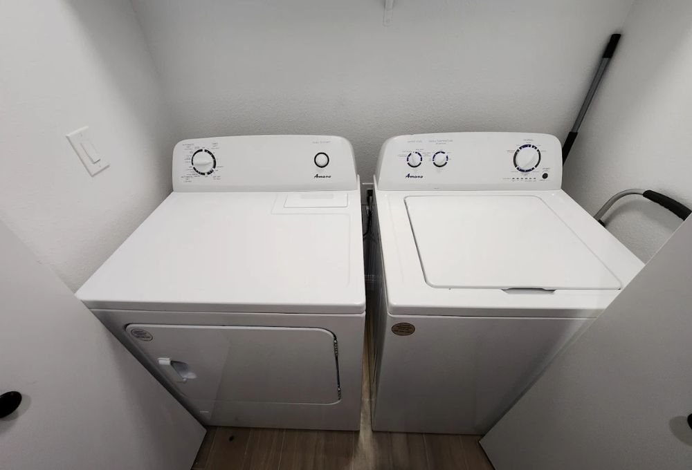 Two white laundry machines (washer and dryer) side by side in a small laundry area.