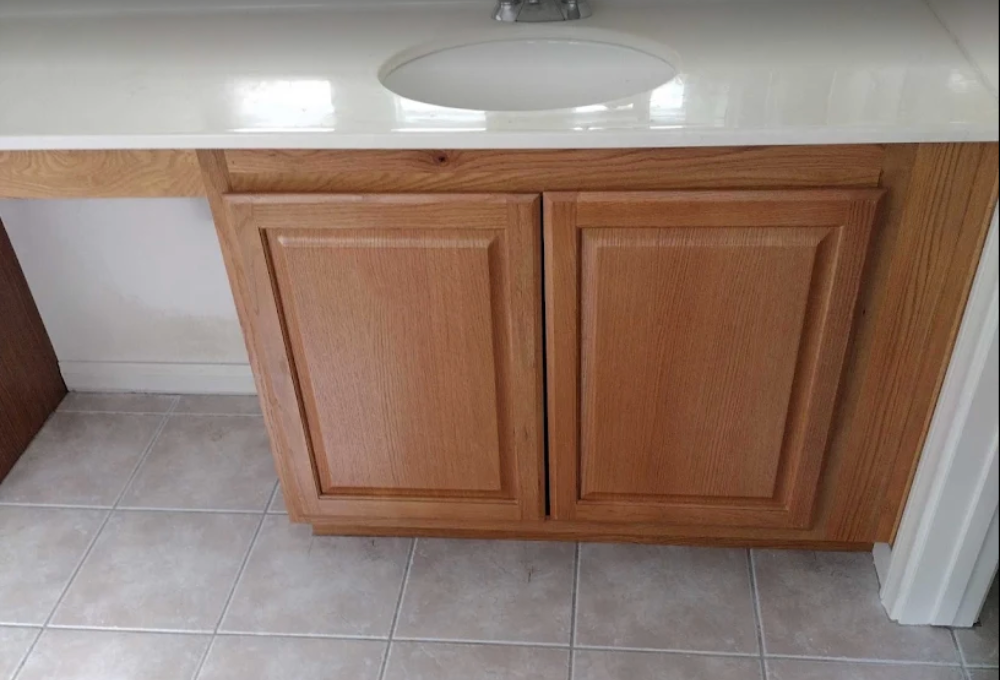 Under-sink cabinet with two wooden doors in a bathroom, beige tiled floor.