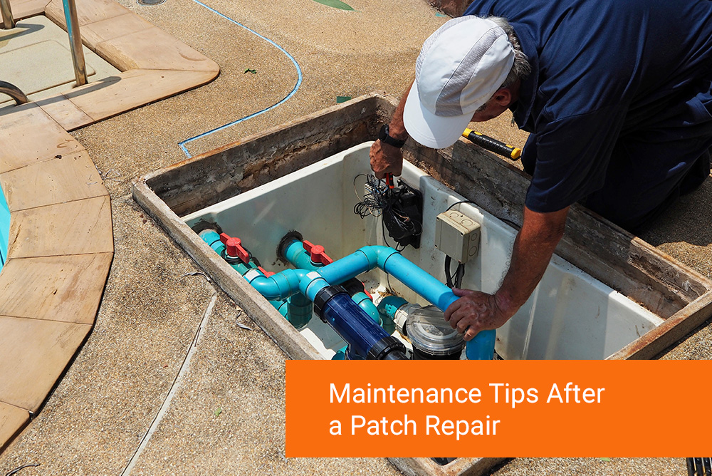 A person in a cap inspects pool equipment in an open maintenance hatch beside a swimming pool.