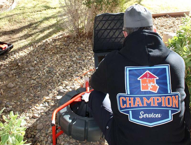 Technician wearing a Champion Service jacket stands outdoors by equipment on a sunny day.