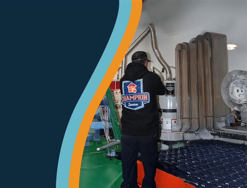 A person in a black hoodie works on a large appliance in a room with pipes and machinery.